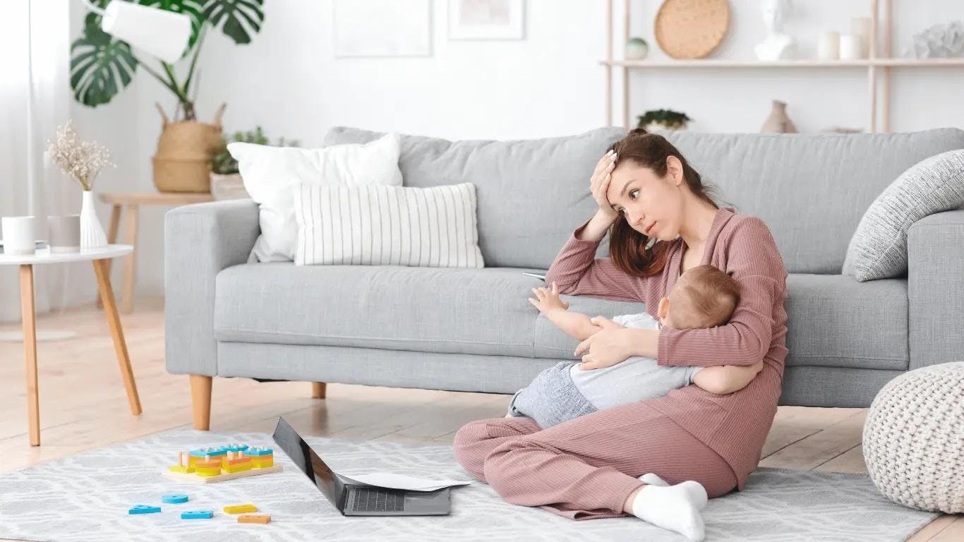 A new mom stares blankly at her computer while trying to balance work with care for her baby.