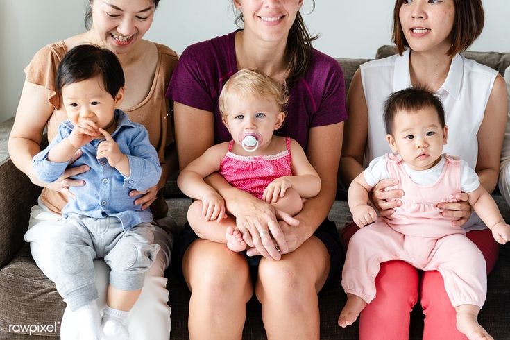 A community of new moms sit on a couch holding their babies.